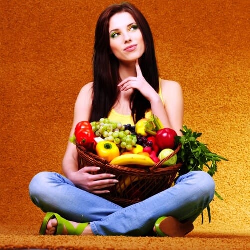A young attractive girl sitting cross-legged on the floor with a basket of fruits in her lap.